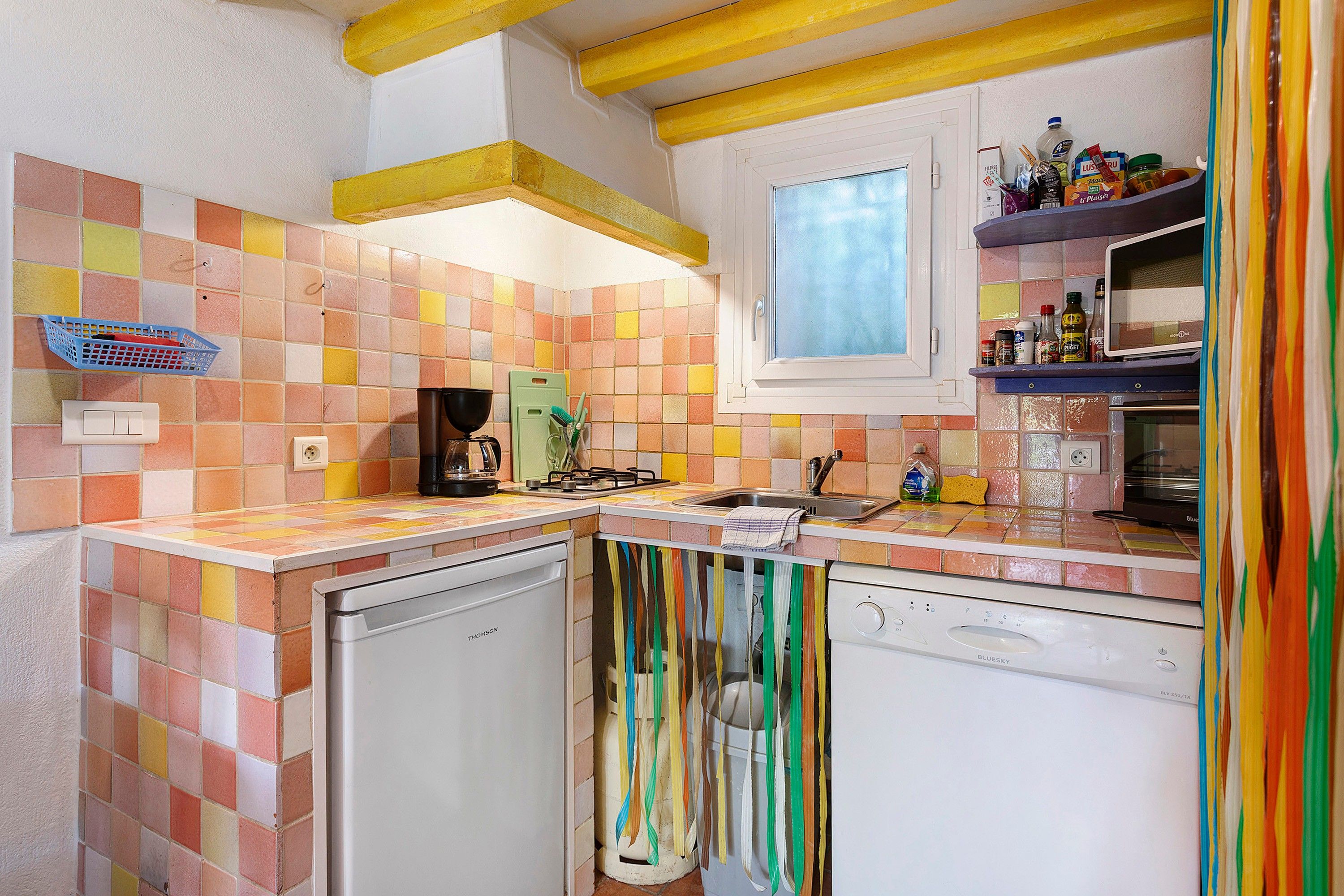 A kitchen with a tiled backsplash, a window, and a microwave on the countertop.