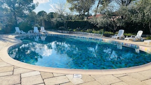 En swimmingpool med flisekant, omgivet af liggestole og en anlagt terrasse.