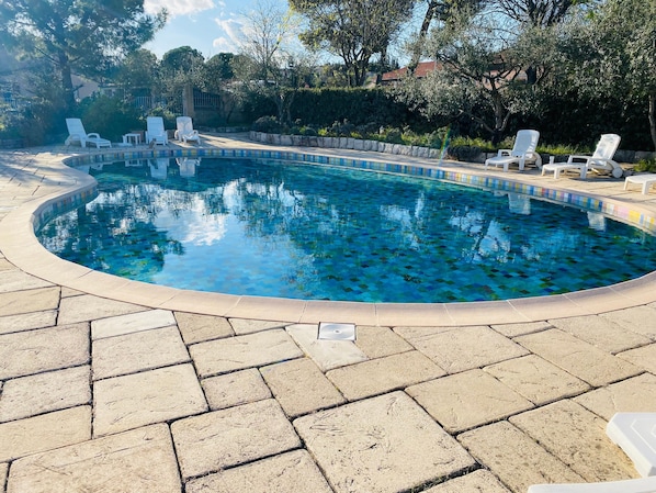 A swimming pool with a tiled edge, surrounded by lounge chairs and a paved deck.
