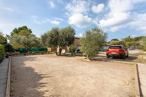 An outdoor parking area with a dirt ground, a yellow hose, and a red car.