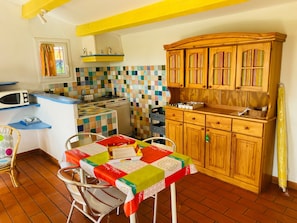 A kitchen with a tiled backsplash, wooden cabinets, a microwave, and a table with a colorful tablecloth.