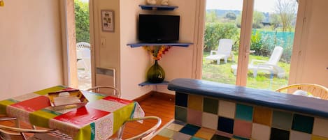 Un comedor con una mesa, sillas, un televisor y vista al jardín a través de la puerta.
