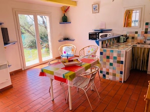 A kitchen with a tiled backsplash, a dining area with a table set for two, and a window with a view of greenery.