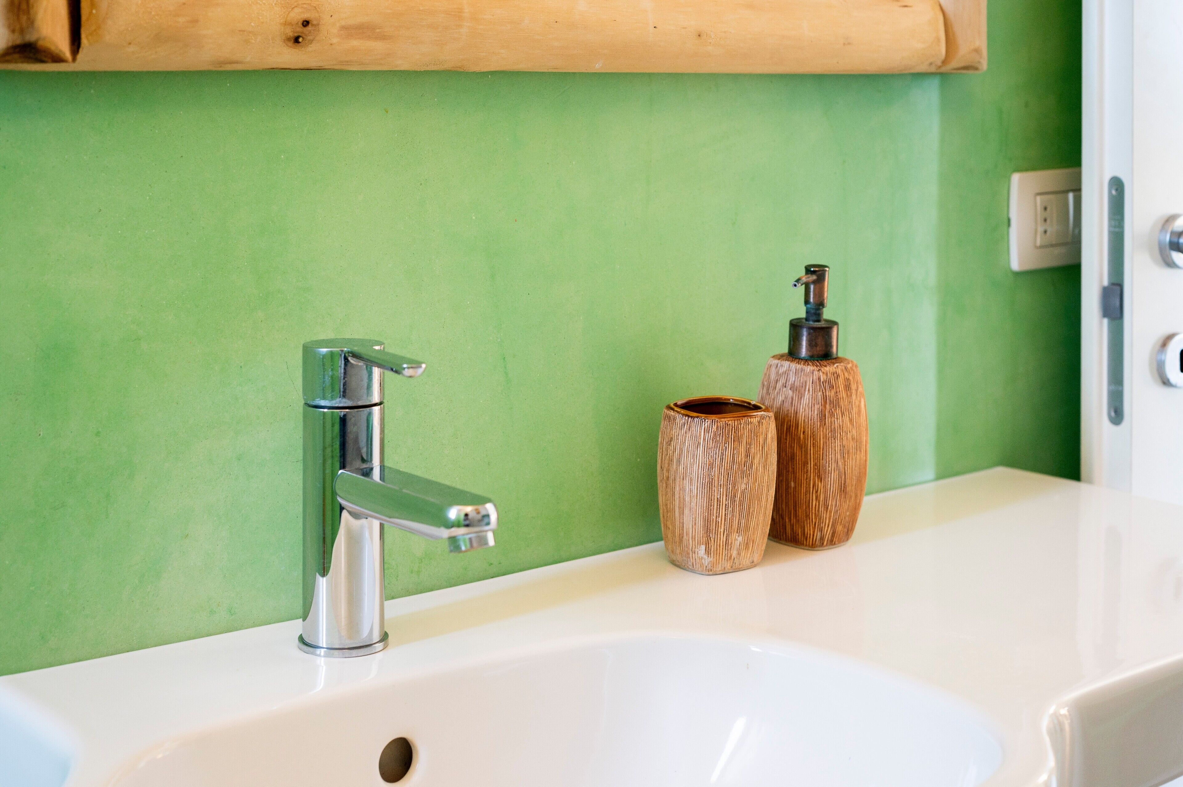 Une salle de bain avec un mur vert, un lavabo blanc, un robinet chromé et deux récipients en bois.