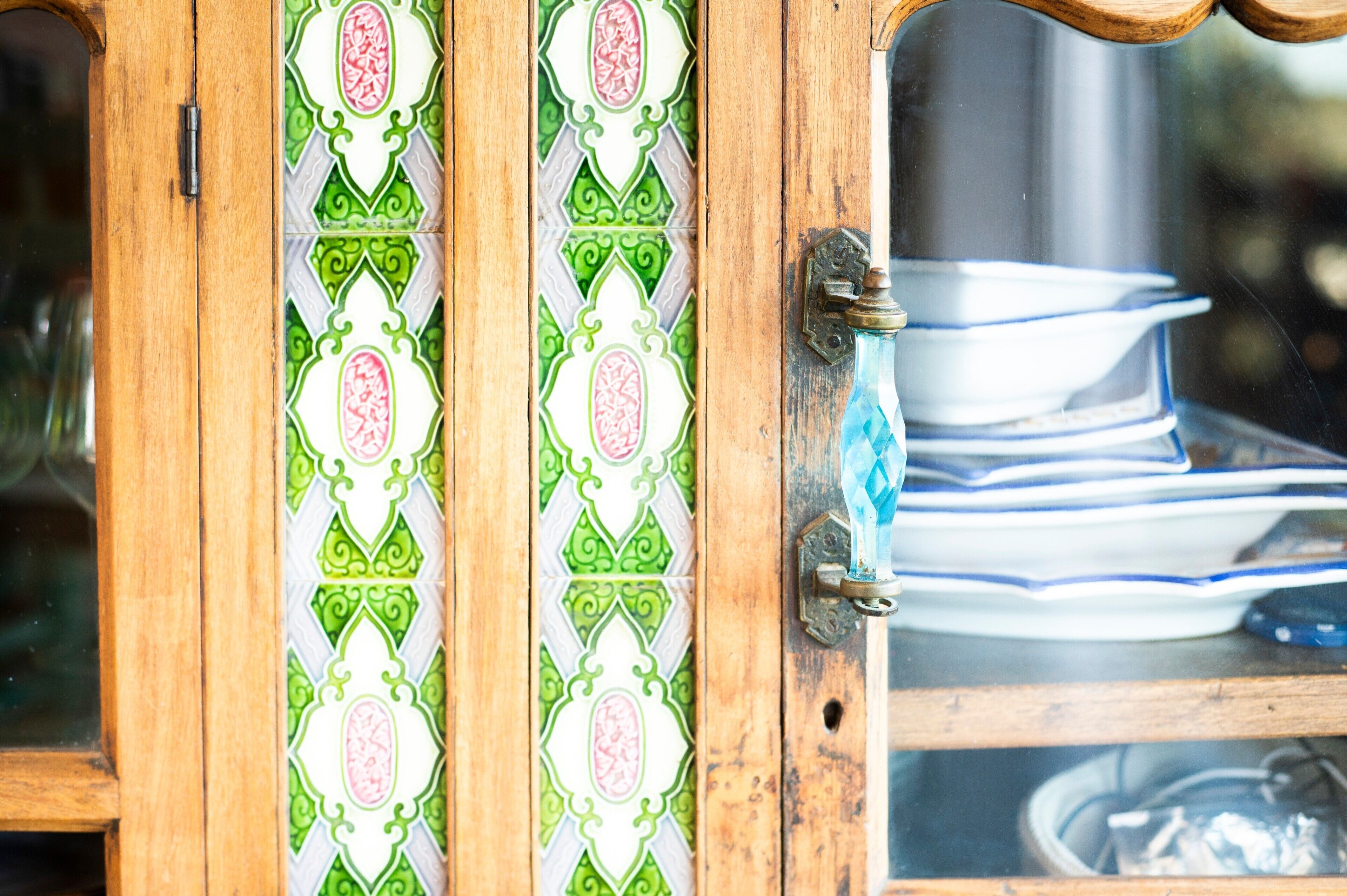 A wooden cabinet with a decorative tile pattern, a brass handle, and stacked white plates inside.