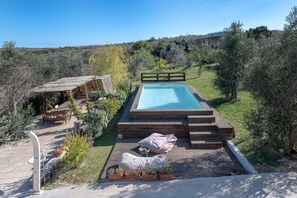 A swimming pool with wooden steps, a wooden deck, and a bench.