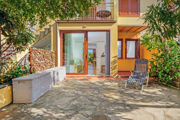 A patio with a stone floor, a white sofa, a metal chair, and a wooden bench.