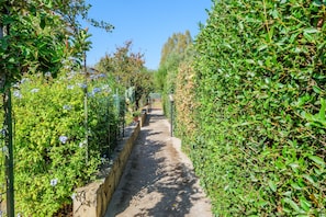 Un sentier bordé d’une végétation luxuriante et de plantes en fleurs, qui mène à une porte.