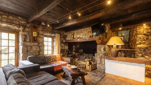 Um interior rústico com lareira de pedra, vigas de madeira, um sofá e uma mesa com abajur.