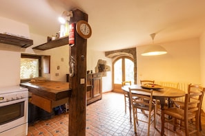 Une cuisine avec une table et des chaises en bois, une horloge et une cheminée en pierre.