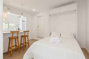 A bedroom with a bed, two wooden stools, a window, and a built-in wardrobe. - Holiday Home "Casita Palmeras" with Mountain View, Private Garden & Wi-Fi (Canyelles)