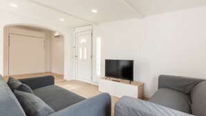 A modern living room with grey sofas, a flat-screen TV on a white cabinet, and a door leading to another room. - Holiday Home "Casita Palmeras" with Mountain Views, Private Garden and Wi-Fi (Canyelles)