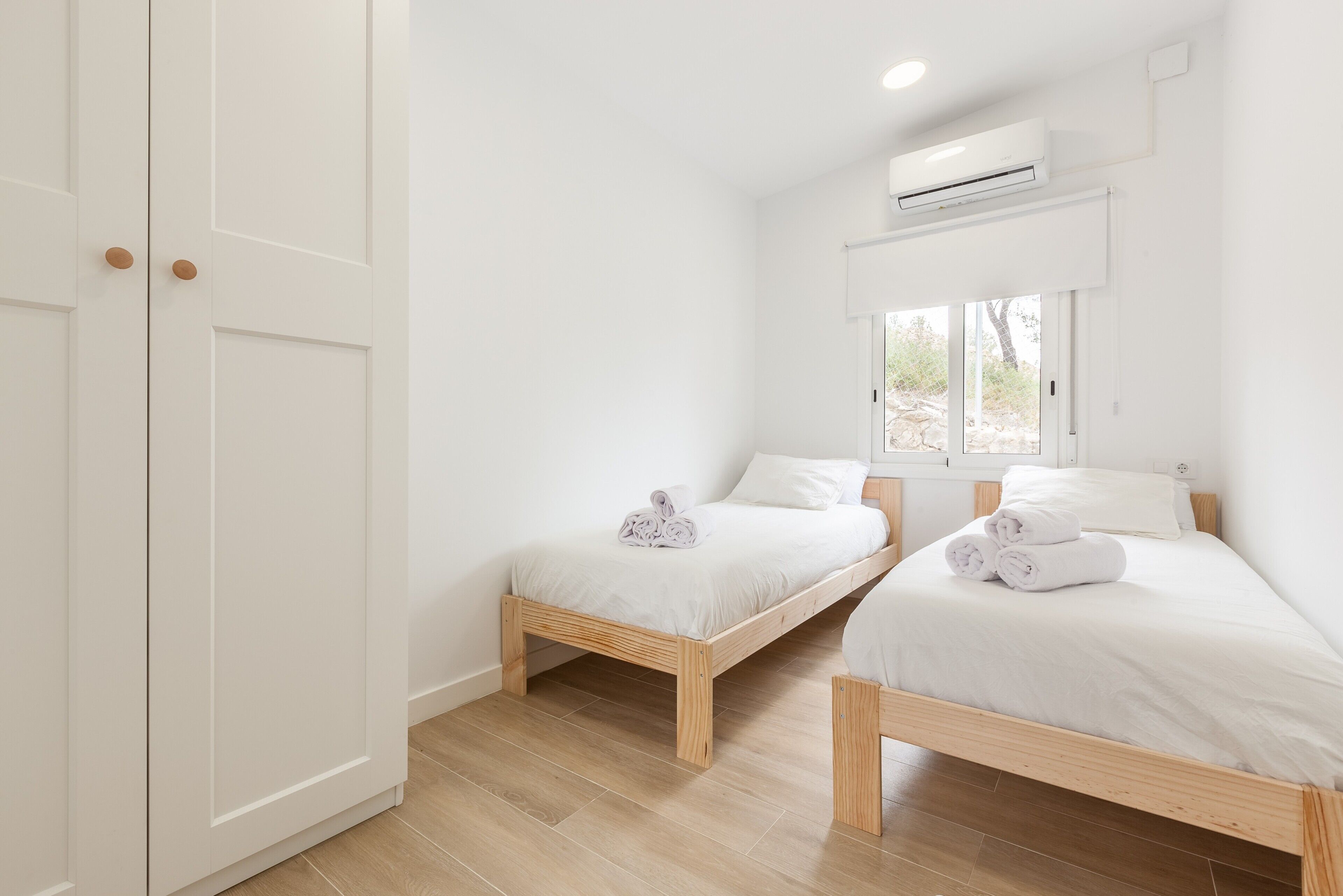 Une chambre avec deux lits, du linge de lit blanc, un plancher en bois et un appareil de climatisation.