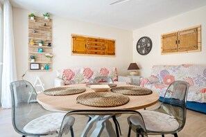 Un espace repas comprenant une table ronde, des chaises transparentes, un canapé et un meuble en bois fixé au mur, doté d ’étagères.
