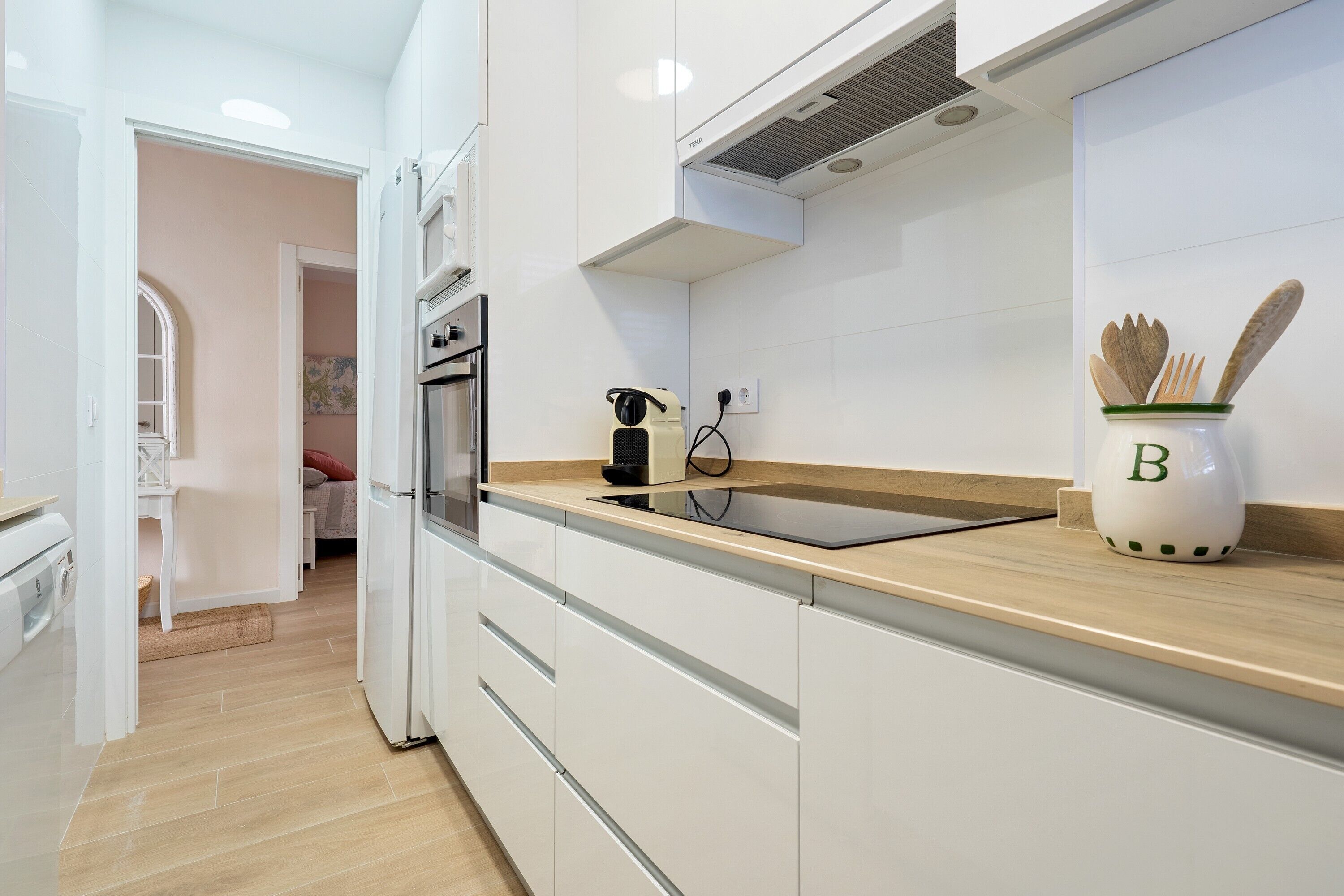 Una cocina moderna con armarios blancos, una encimera de madera y una cafetera.