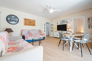 Un salon comprenant un canapé, une table à manger avec des chaises, un téléviseur et un ventilateur de plafond.