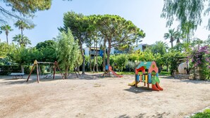 Ein Spielplatz mit Schaukeln und Rutschen, umgeben von Bäumen und Gebäuden.