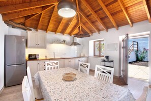 Una cucina con soffitto in legno, mobili bianchi, un frigorifero e un tavolo da pranzo con sedie.