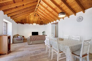 Un comedor con techo de madera, sillas blancas, una mesa con mantel estampado y un reloj en la pared.