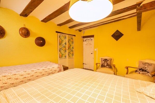 A room with yellow walls, a bed with a patterned bedspread, a chair with a cow pillow, and a wooden ceiling. - Holiday Home "Cal Barral" with Mountain View, Balcony & Wi-Fi (Ansovell)