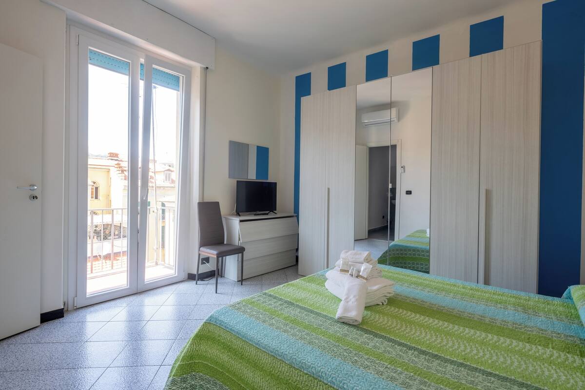 Habitación de hotel con cama, escritorio con computadora, una silla, televisor y puerta corredera al balcón.