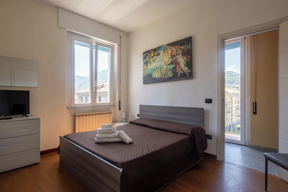 Un dormitorio con cama, cómoda, un cuadro y vistas al exterior.