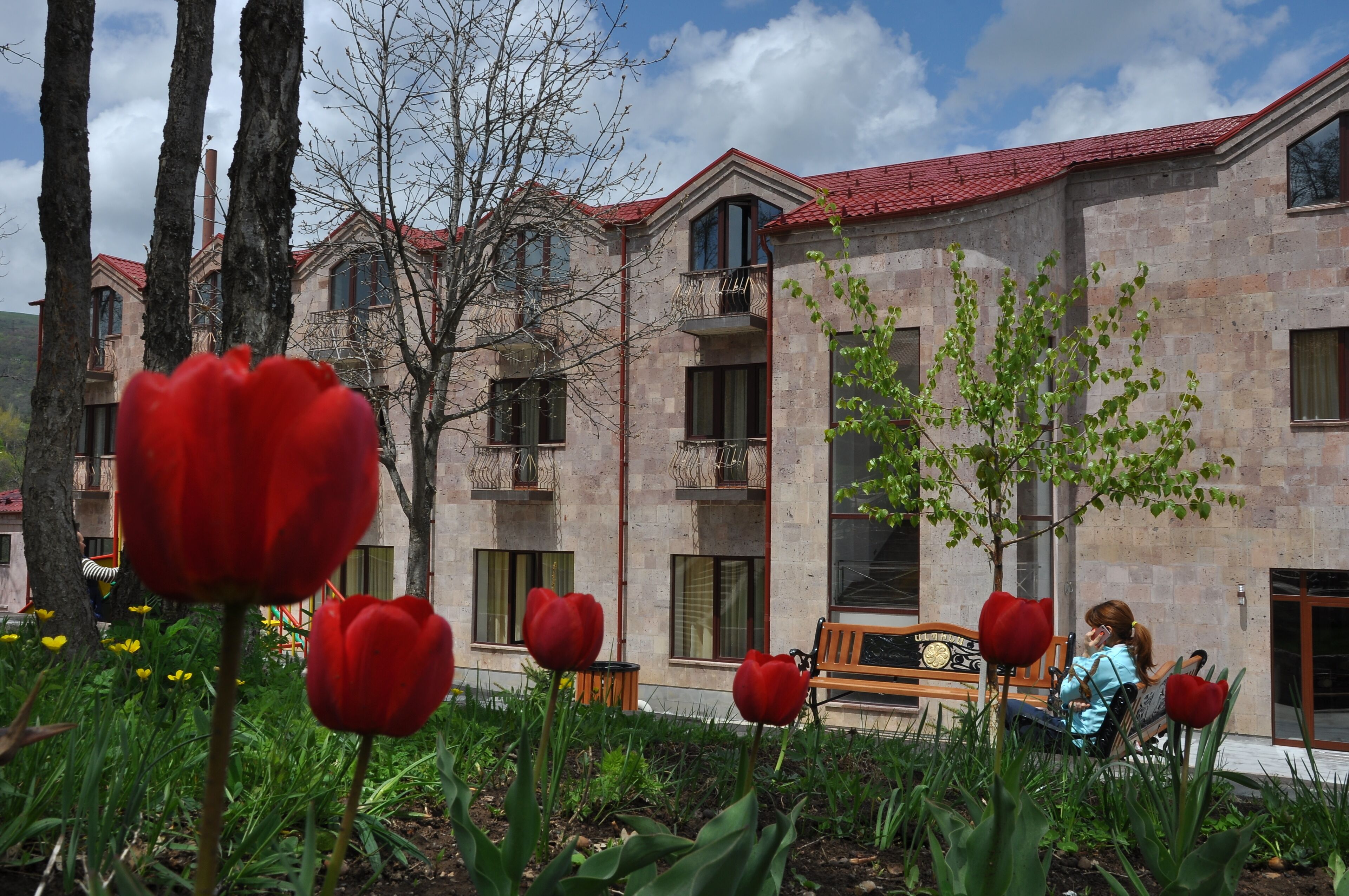 A building with a red roof and multiple windows, surrounded by greenery and red tulips.