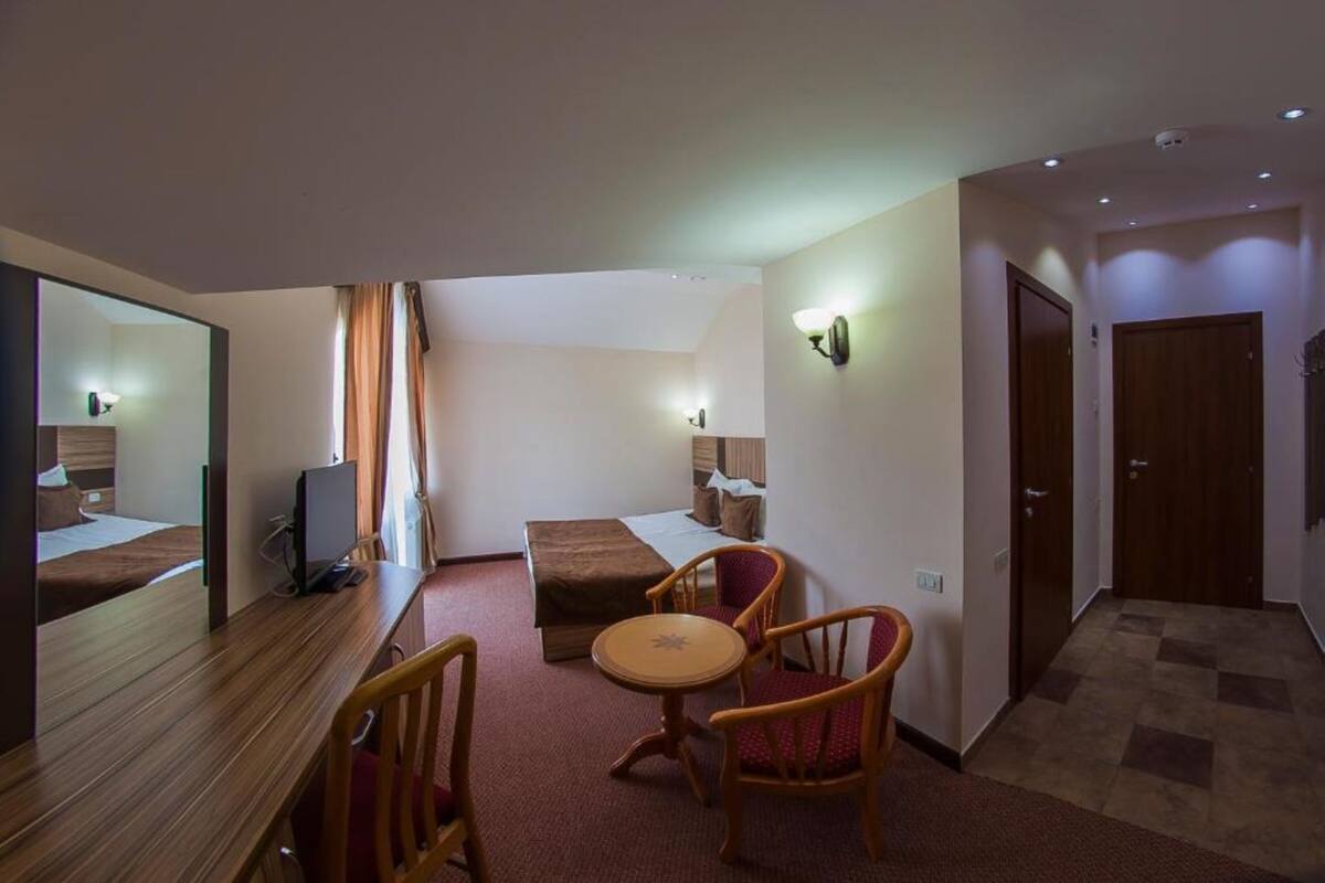 Habitació d'hotel amb escriptori de fusta, dues cadires, taula rodona petita, llit, televisió i mirall.