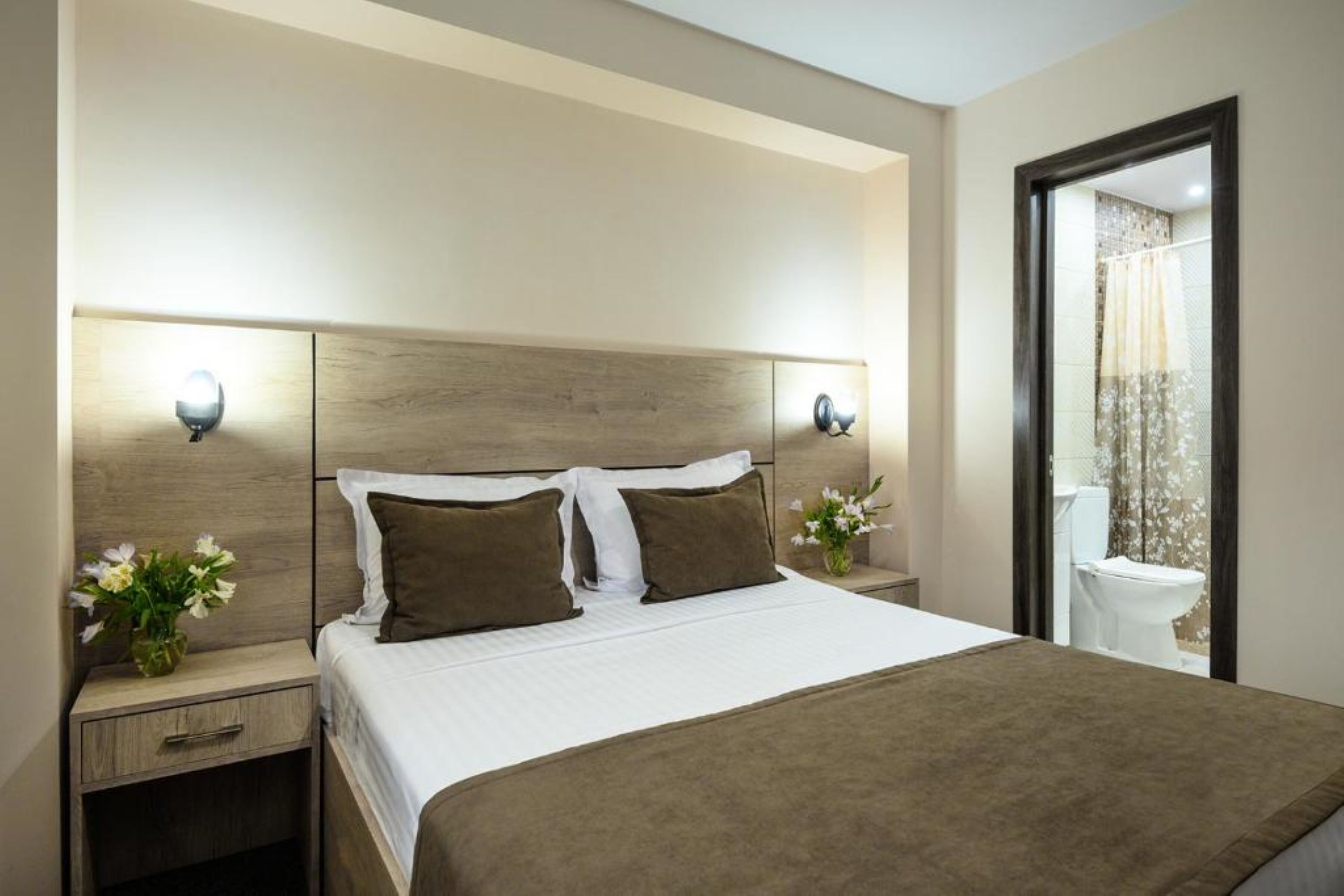 Habitación de hotel con una cama grande, dos mesitas de noche y un baño visible a través de una puerta abierta.