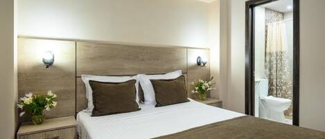 Habitación de hotel con una cama grande, dos mesitas de noche y un baño visible a través de una puerta abierta.