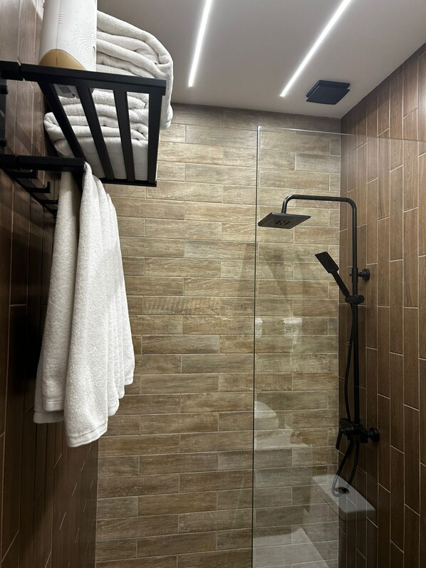 A modern bathroom with a glass shower enclosure, wooden wall tiles, and a towel rack with folded towels. - Alpina Resort by Stellar Hotels, Tsaghkadzor (Tsaghkadzor)