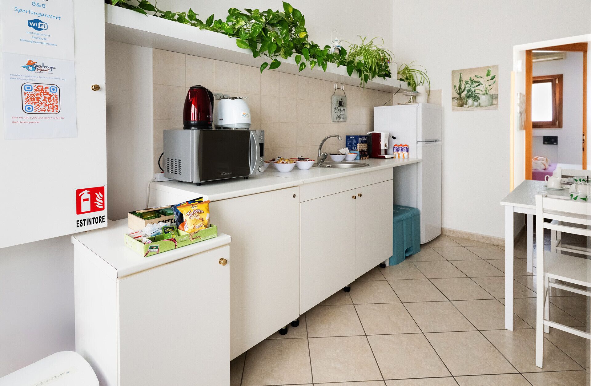 A compact kitchenette with a microwave, kettle, and coffee maker. There is a small refrigerator, a sink, and a window with a view of the garden.