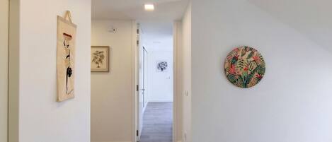A hallway with a wooden floor, white walls, and artwork including a framed picture and a circular wall hanging.