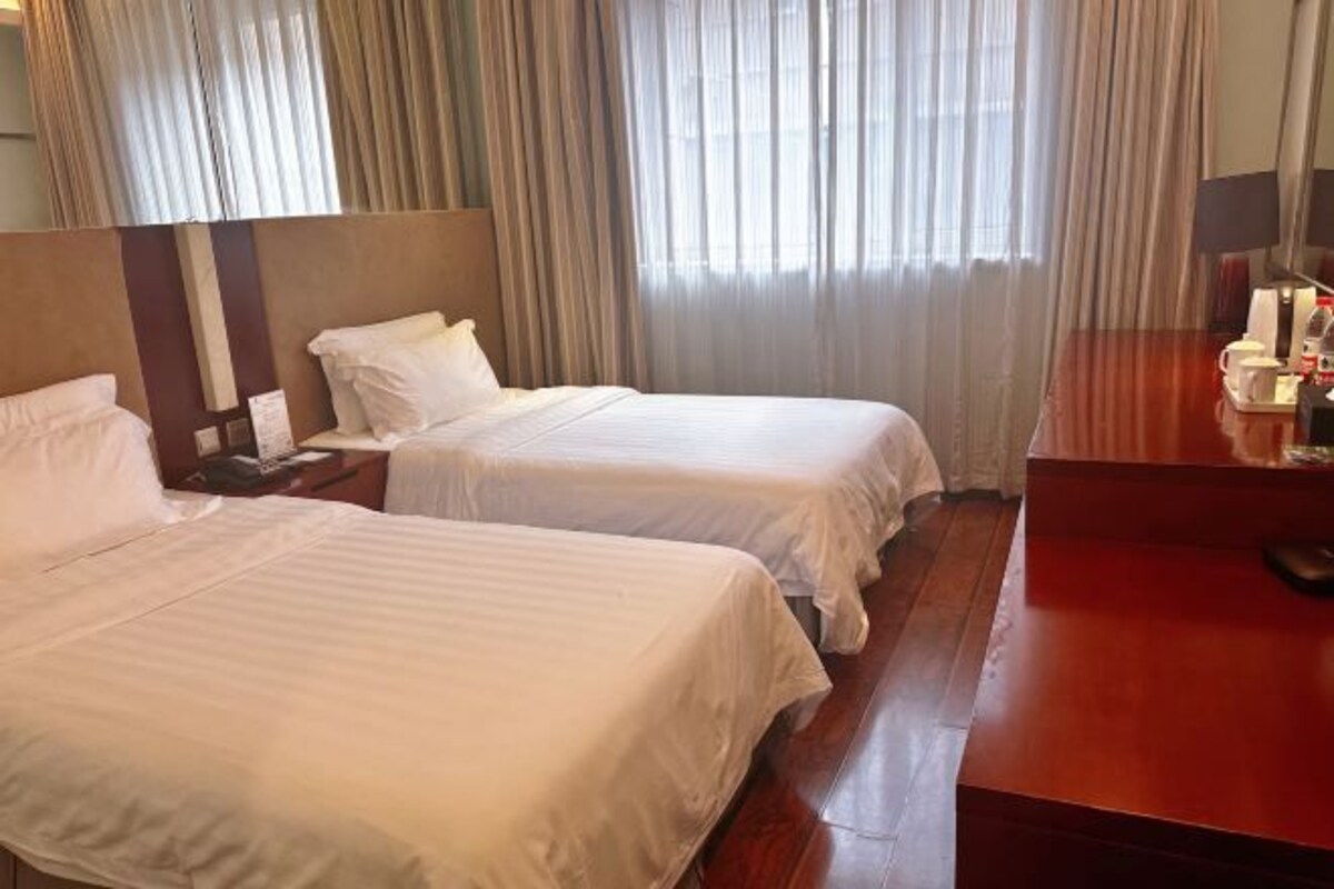 Camera d'albergo con due letti, una scrivania in legno, un comodino e un'ampia finestra con tende.