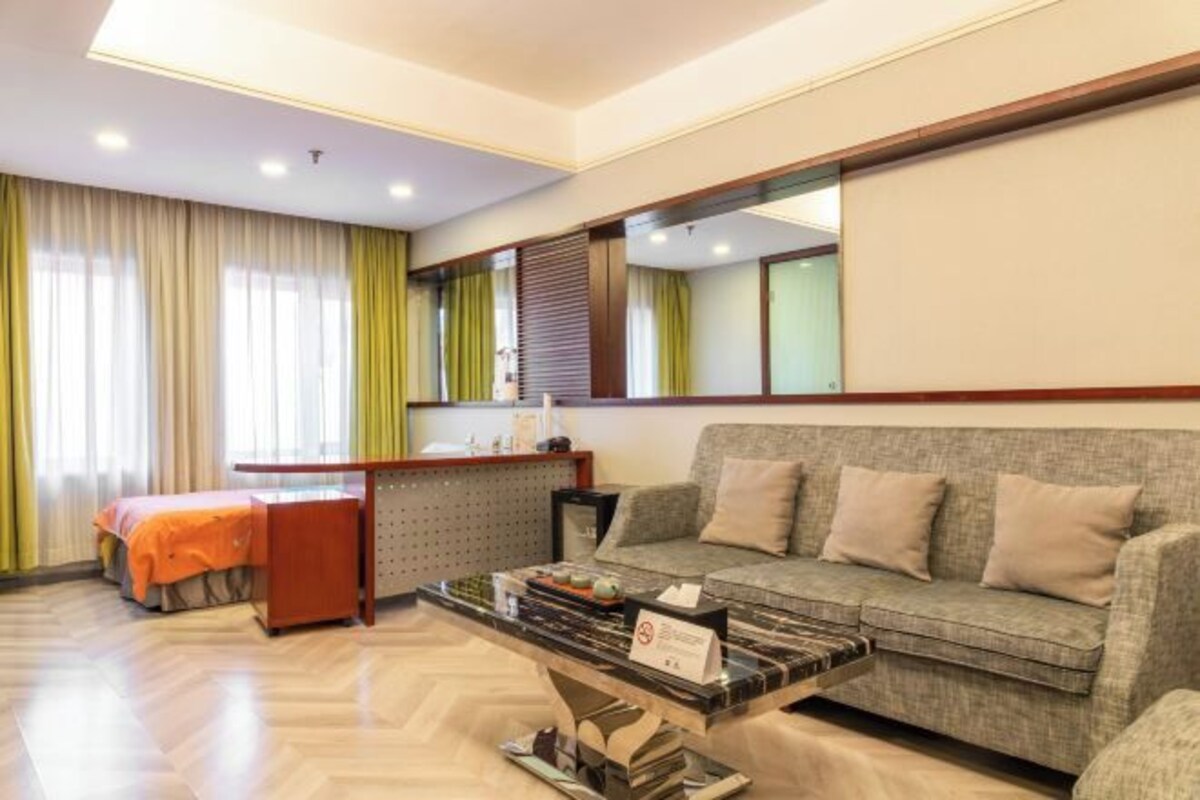 Una camera d'albergo con un divano, un tavolino, una scrivania con una sedia e un letto con coperta arancione.