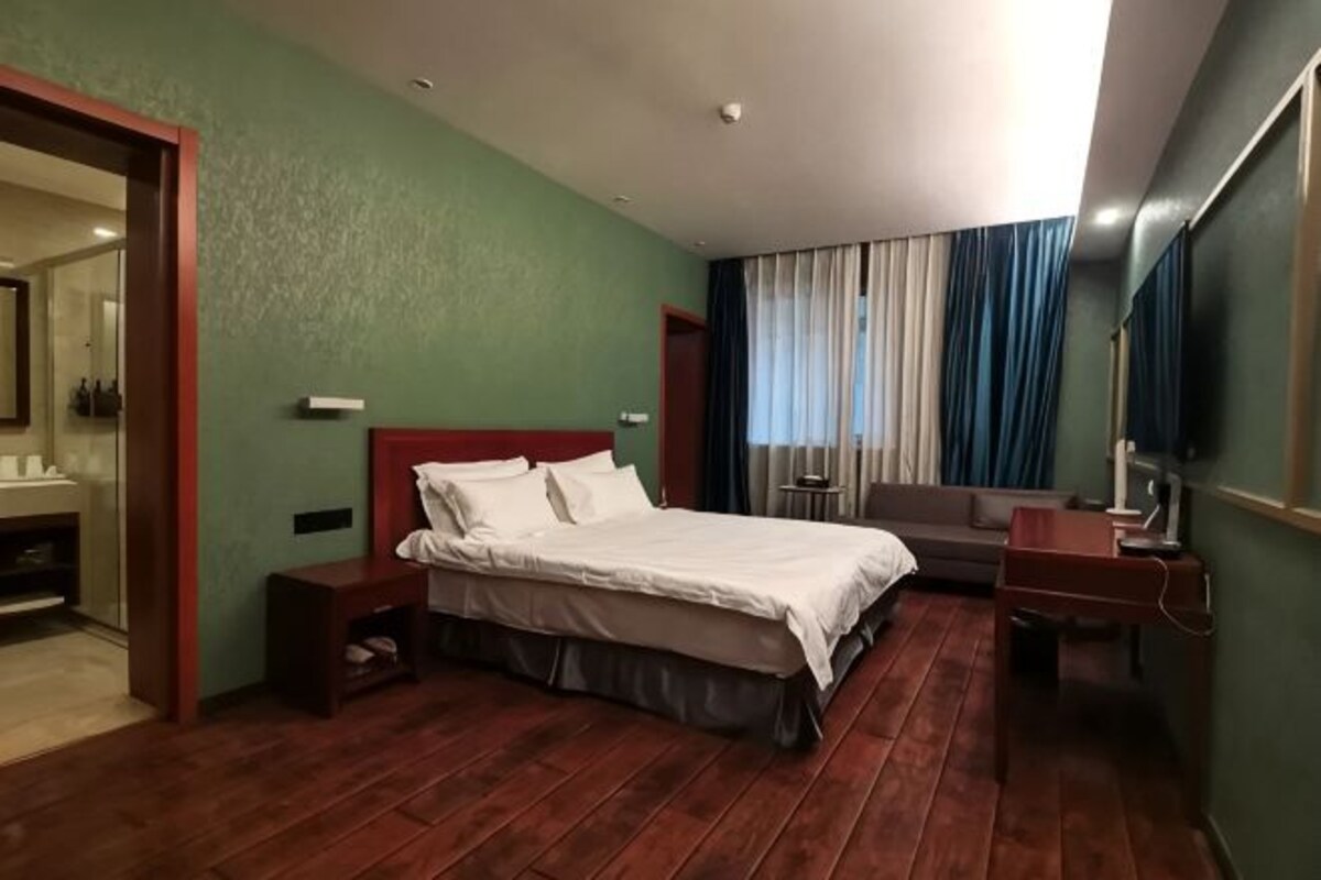 Una camera d'albergo con un letto, una scrivania, uno specchio e una finestra con tende.