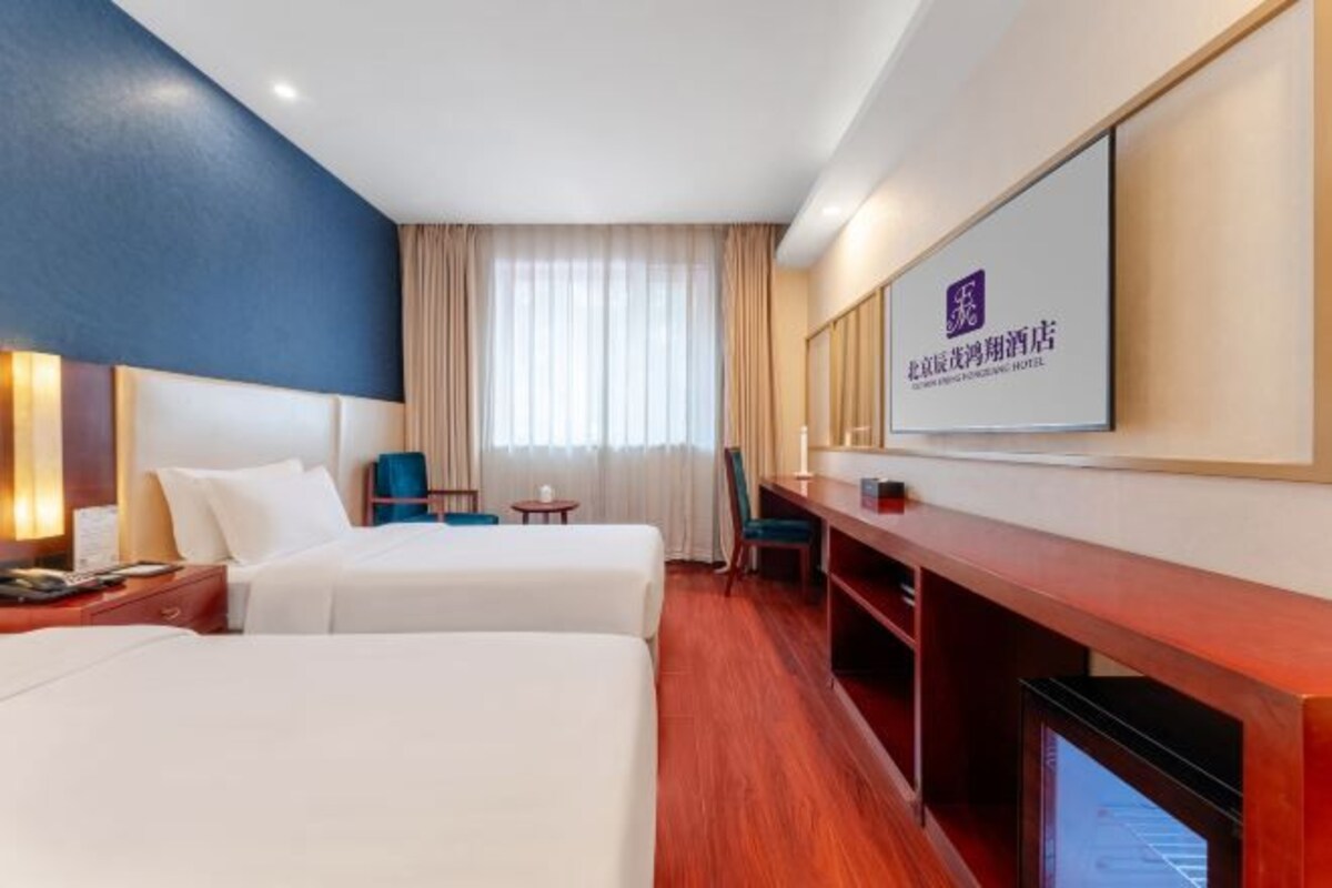 Camera d'albergo con due letti, una scrivania, una sedia, una televisione e una grande finestra con tende.