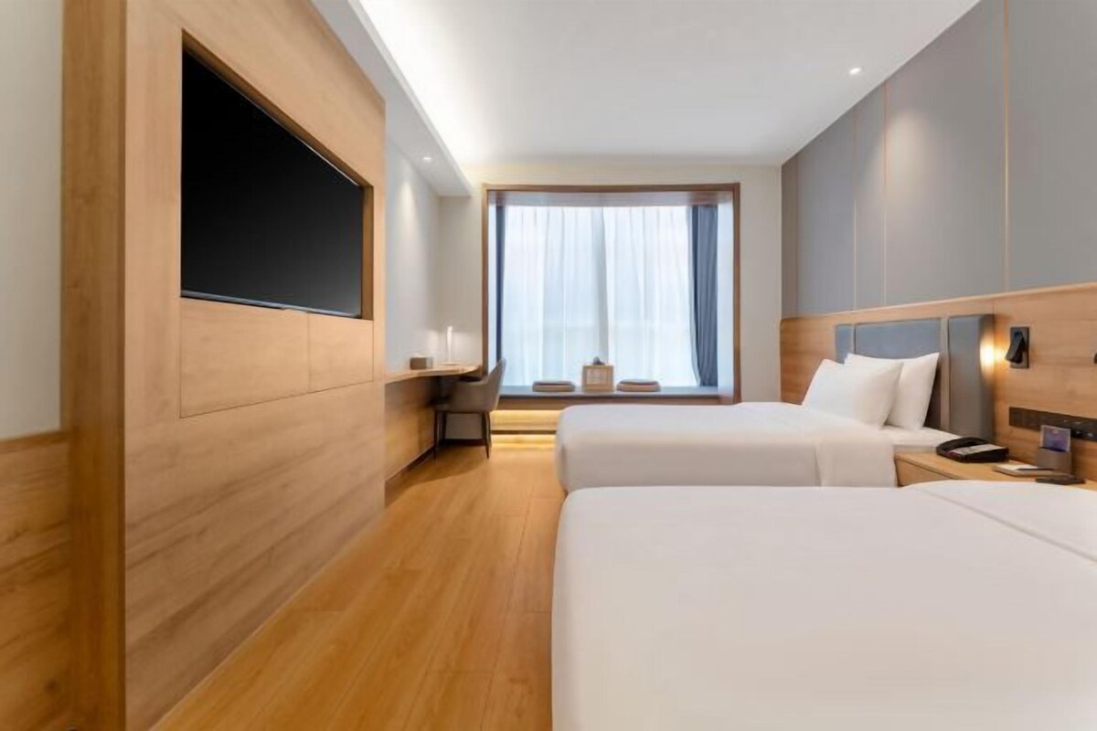 Une chambre d’hôtel avec deux lits, un bureau, une télévision et une grande fenêtre avec des rideaux.