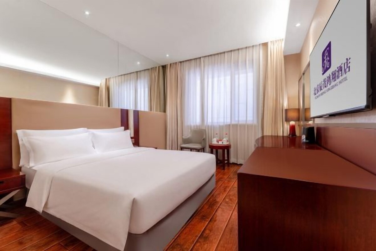 A hotel room with a large bed, a desk, a chair, and a TV.