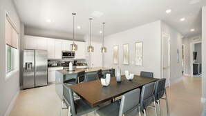 A modern kitchen with stainless steel appliances, a dining area with a wooden table and chairs, and pendant lighting.