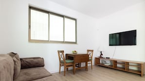 Ein Wohnzimmer mit braunem Sofa, einem Holzesstisch mit zwei Stühlen, einem an der Wand montierten Fernseher und einer Holzbank.