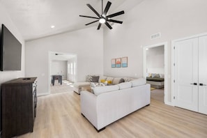 A spacious living room with a large sofa, a dark wooden cabinet, and a ceiling fan.