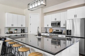A modern kitchen with white cabinets, a large island with stools, stainless steel appliances, and a pendant light fixture.