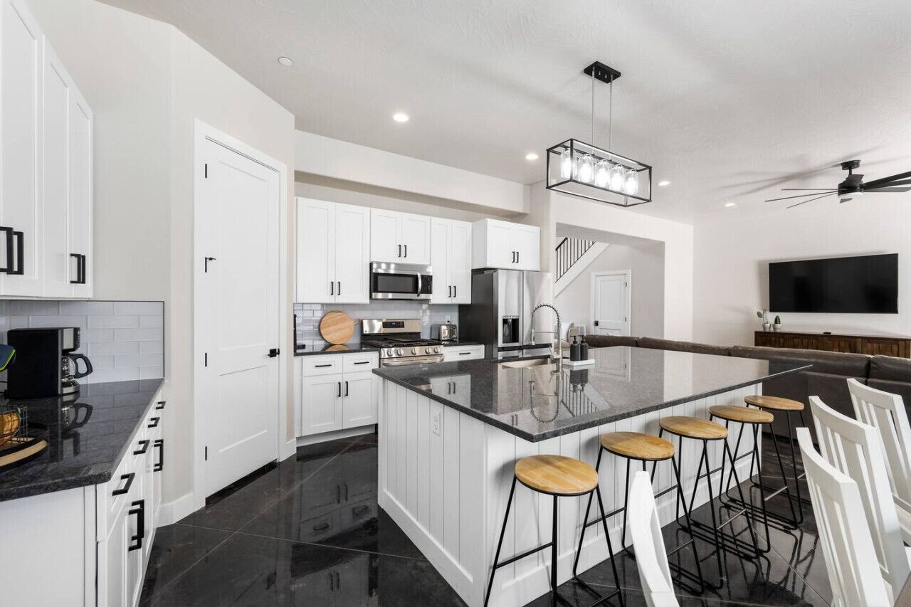A modern kitchen with white cabinetry, a central island with stools, a built-in oven, and a large TV mounted on the wall.