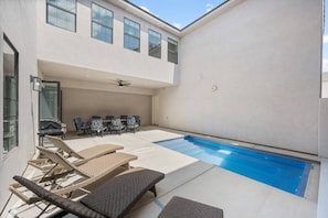A modern outdoor pool area with lounge chairs and a table, surrounded by a white building with large windows.