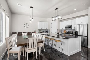 A modern kitchen with white cabinetry, a central island with stools, and a dining area with a large table and chairs.