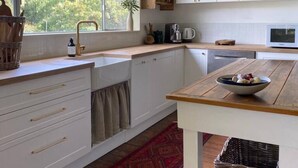 Une cuisine avec des meubles blancs, un plan de travail en bois, un tapis rouge et une vue sur les arbres à l’extérieur.