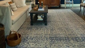 Un salon avec un mur d’accent bleu foncé, une grande armoire en bois, un lustre, un canapé, deux fauteuils, une table basse et un tapis à motifs.