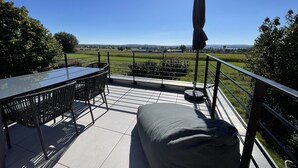 A terrace with a table and chairs, a cushioned bench, and a view of the countryside.