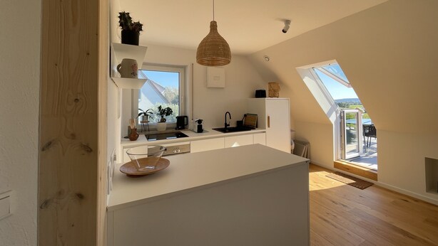 A modern kitchen with a central island, a hanging light fixture, and a view of the outdoors through a skylight.
